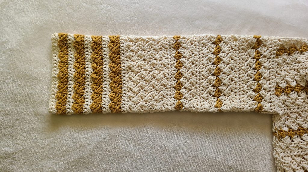 "Textured crochet sleeve in yellow and beige stripes, displayed on a white background, evoking a cozy, handmade feel."