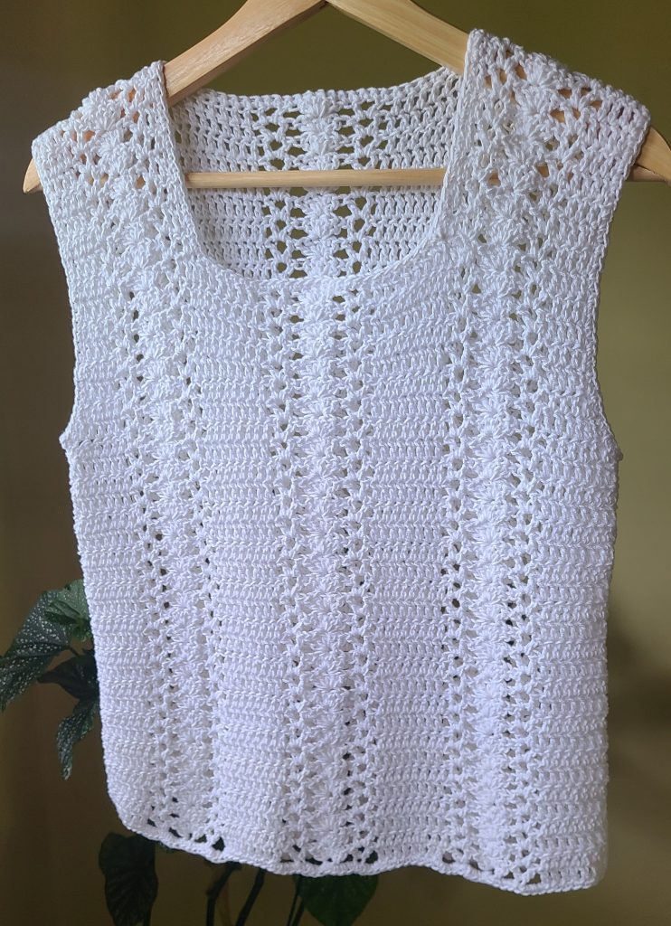 Handmade sleeveless crochet lace top with lace stitches hanging on a hanger