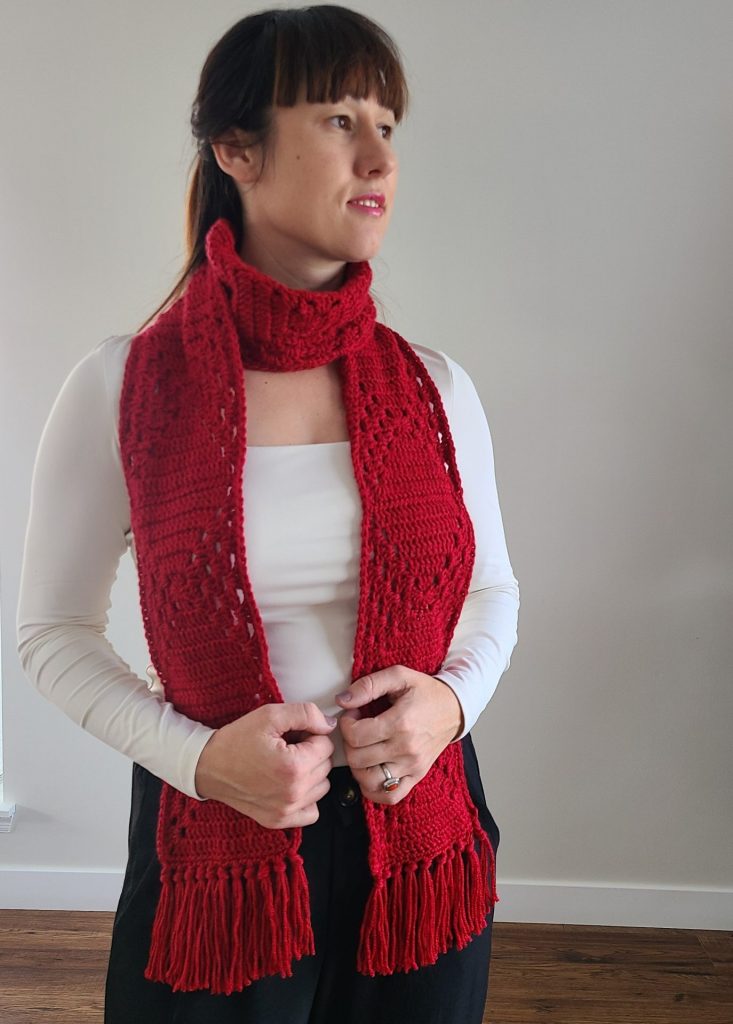 A woman wearing a red crochet granny square scarf on a white background.