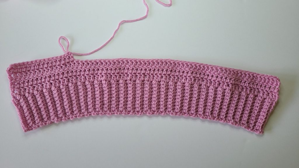 Close-up of crochet pink cozy vest back panel showing stitch details on white background.