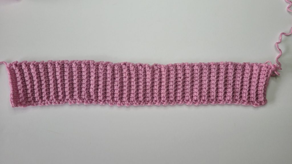 Detailed view of ribbing stitches on the crochet pink cozy vest back panel displayed on white background.