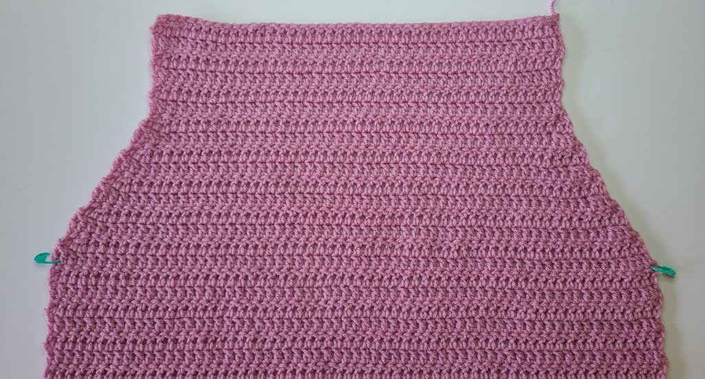 Close-up of crochet pink cozy vest back panel showing stitch details on white background.