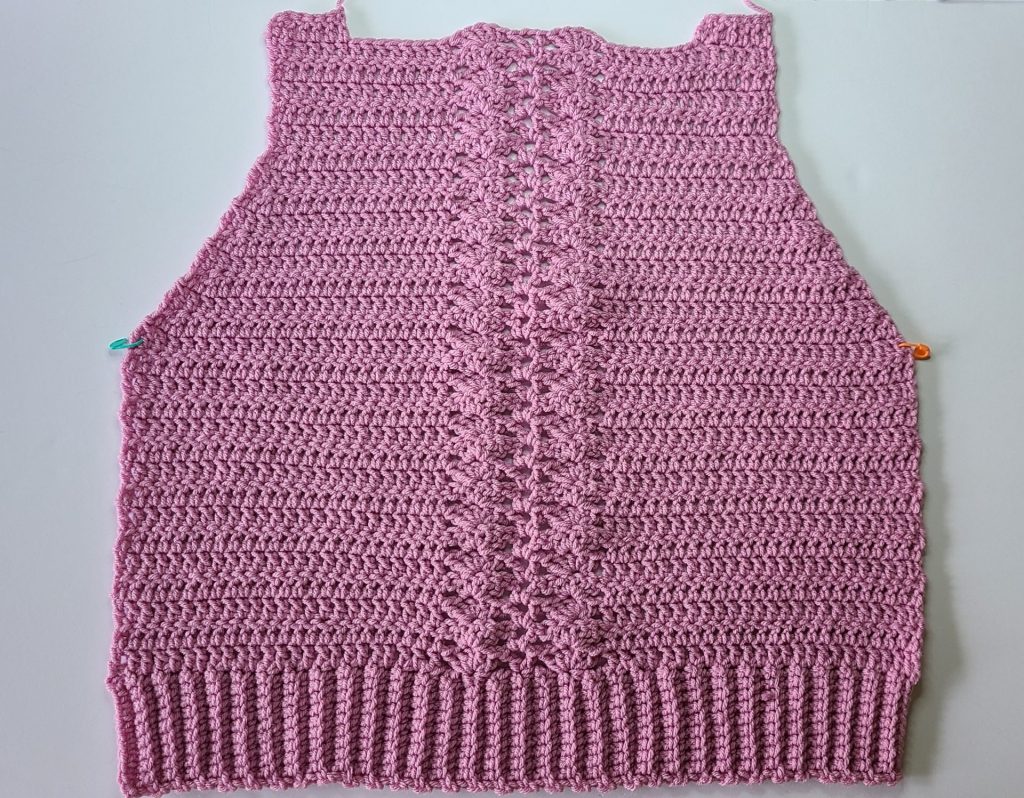 Finished crochet pink cozy vest front panel ready for assembly, shown on white background.