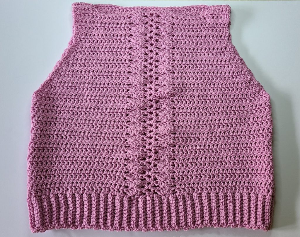 Flat lay of crochet pink cozy vest with front and back panels connected on clean white background.