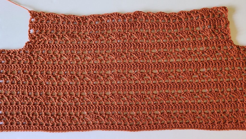 A long rust-colored crochet lace panel laid flat, showing repeating openwork stitch rows.