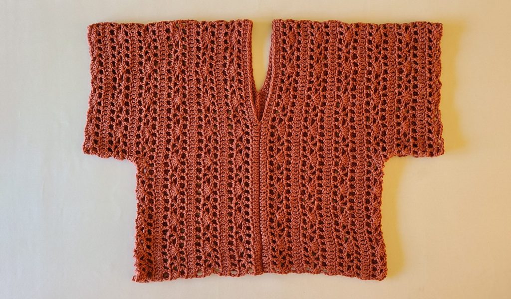 Rust-colored crochet lace top laid flat, showing repeating openwork stitch rows.
