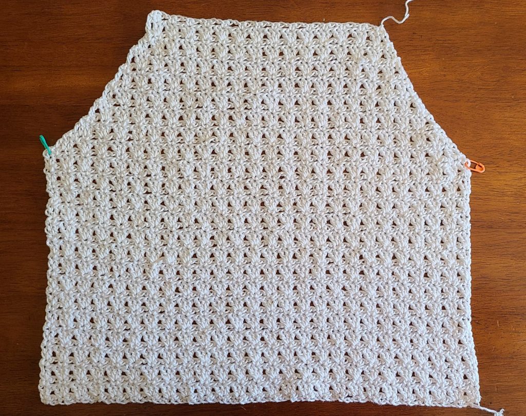 Crochet top panel worked in parquet stitch, made from a written crochet pattern, showing armhole and neckline shaping for garment construction, laid flat on a wooden surface with stitch markers.