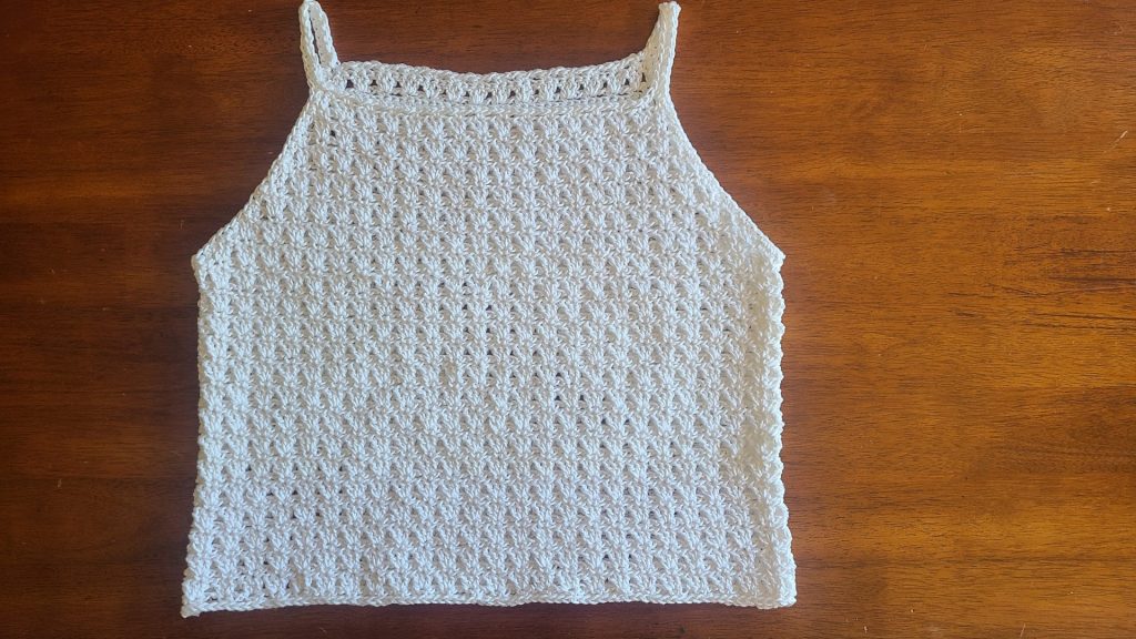 Flat lay of a crocheted top panels worked in a textured stitch pattern, shown after shaping for the armholes and neckline, laid on a wooden surface with stitch markers on each side.
