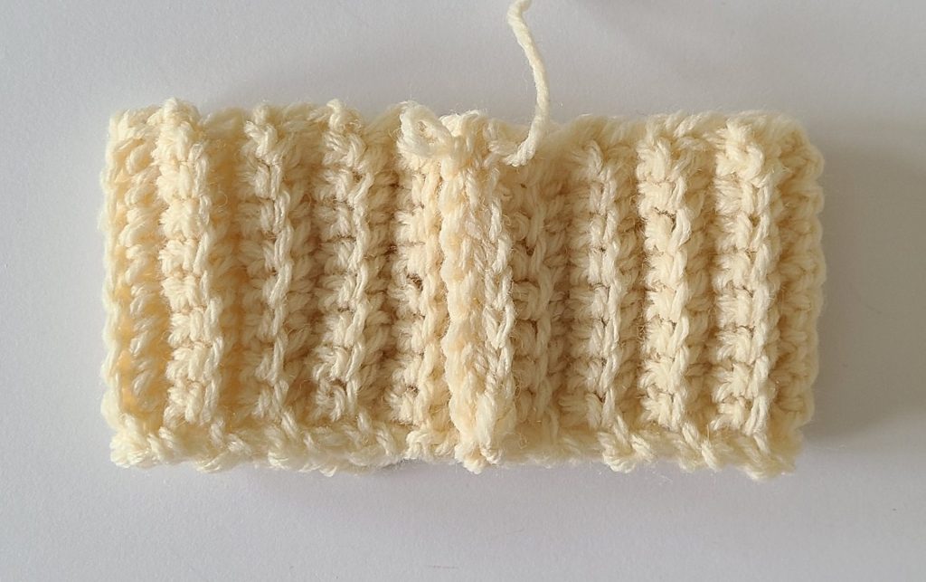 One beige half crochet leg warmer displayed on a flat white background, showing texture and stitch details, the bottom ribbing folded by slip stitch.