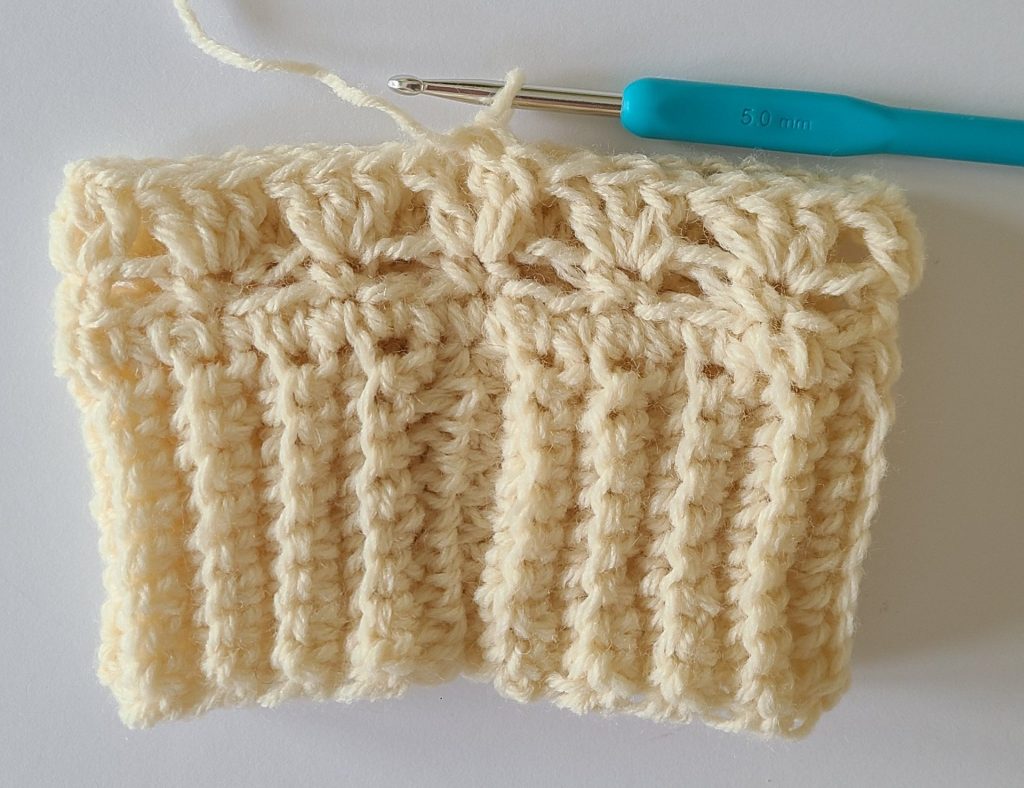 One beige half crochet leg warmer displayed on a flat white background, showing texture and stitch details, the bottom ribbing and and the first 3 rows.