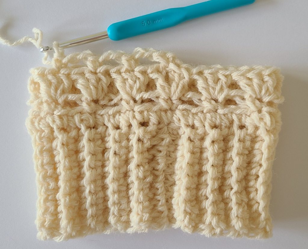 One beige half crochet leg warmer displayed on a flat white background, showing texture and stitch details, the bottom ribbing and and how to start rows 4.