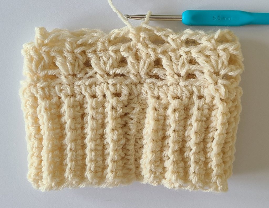 One beige half crochet leg warmer displayed on a flat white background, showing texture and stitch details, the bottom ribbing and and how to finish rows 4.