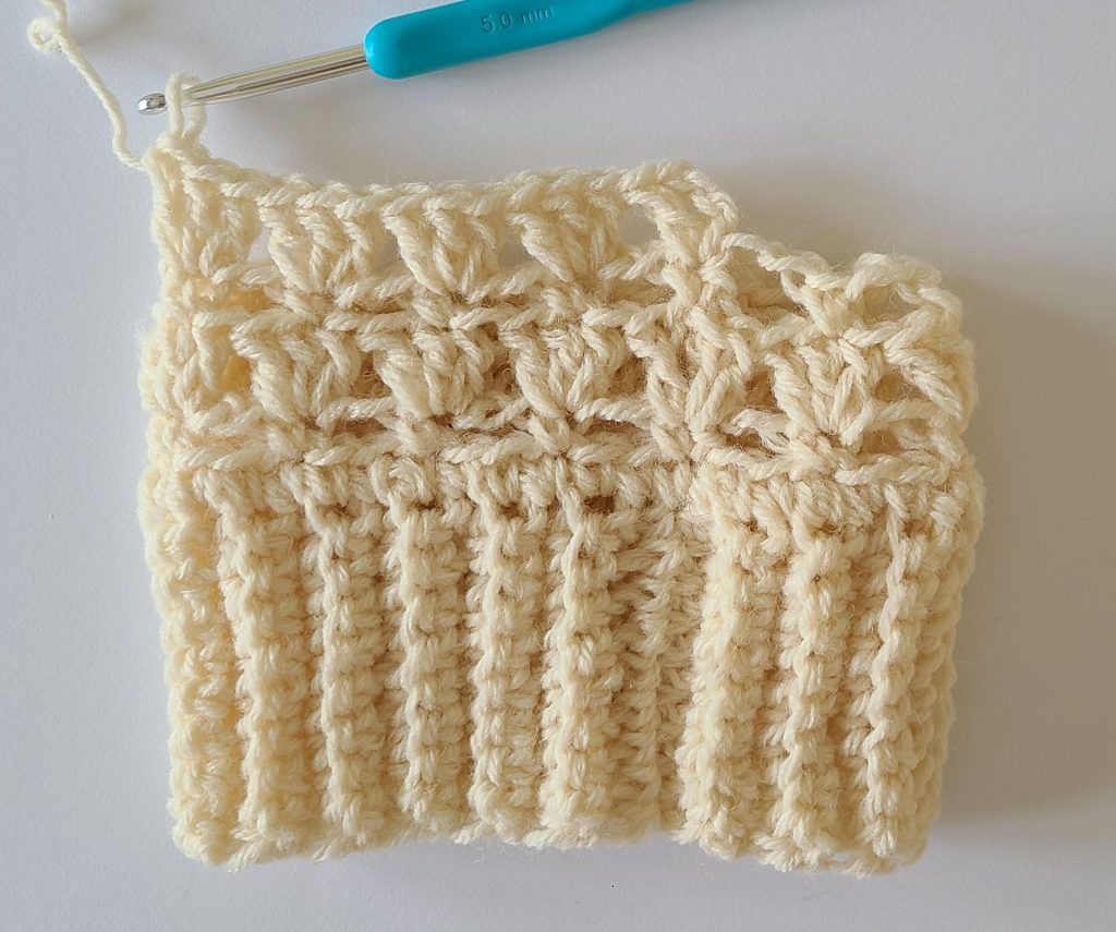 One beige half crochet leg warmer displayed on a flat white background, showing texture and stitch details, the bottom ribbing and and how to start rows 5.