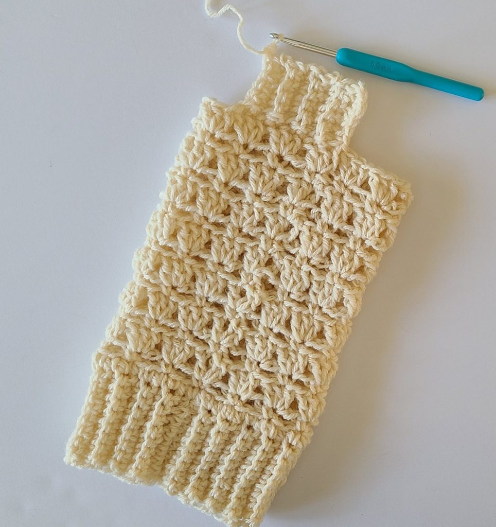 One beige crochet leg warmer displayed on a flat white background, showing texture and stitch details starting the top ribbing 