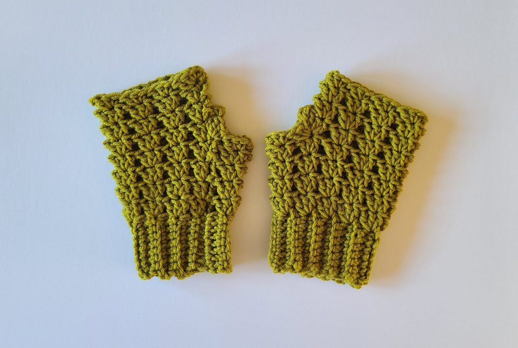 "Olive green cozy crochet fingerless gloves laid flat on a white background, showing the full shape, ribbed texture, and stitched edges, highlighting the overall design and craftsmanship."