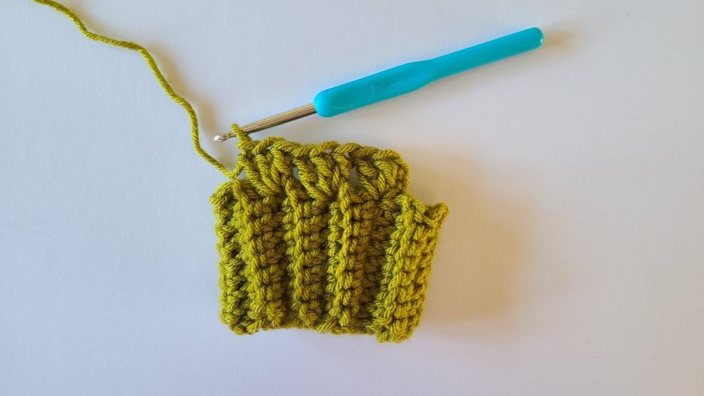 Close-up of olive green crochet fingerless gloves, highlighting the ribbed texture of the fabric and clearly showing the start of row 1, with stitches and rows visible for reference