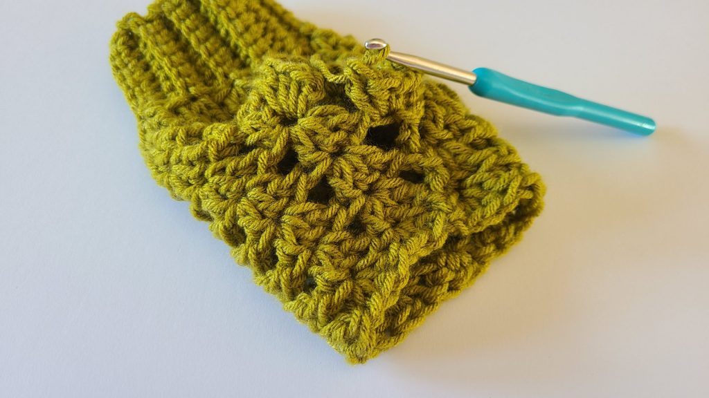 "Olive green crochet fingerless glove flat on a white background, showing the thumb border."