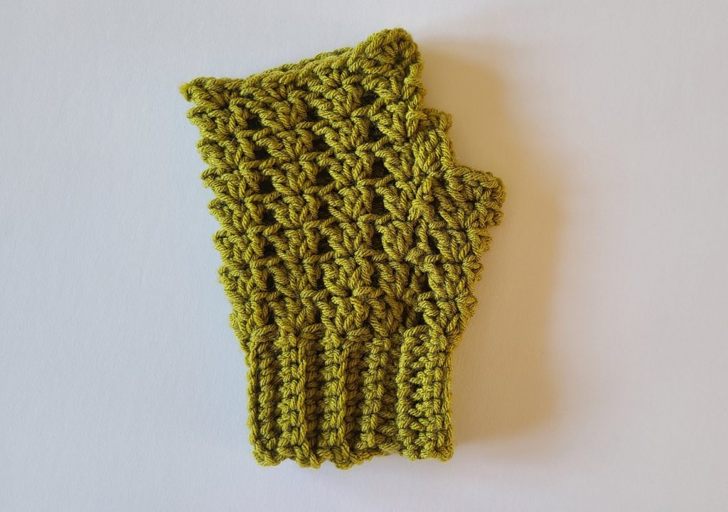 "Olive green crochet fingerless glove laid flat on a white background, showing the textured ribbing, stitch details, and overall shape of the glove."