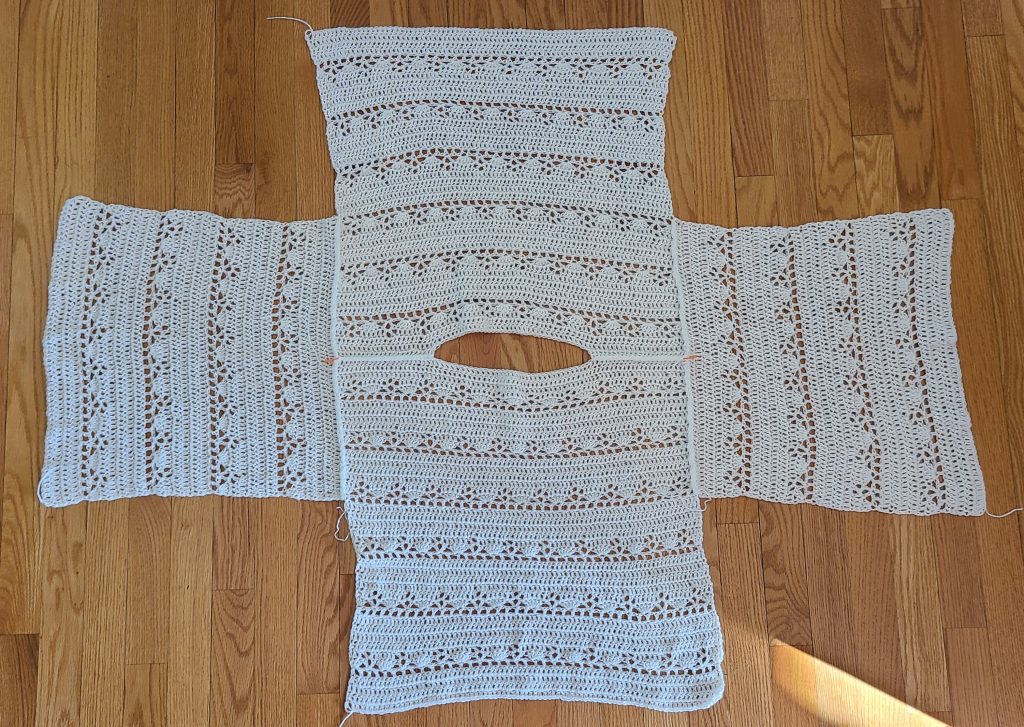 All crochet lacy sweater panels laid flat, including front, back, and sleeves, before assembly