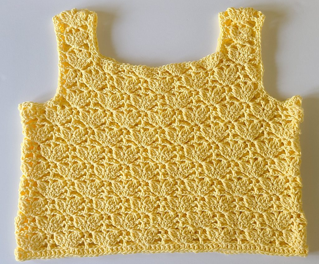 Finished yellow Lorelay crochet crop top with textured stitch pattern flat on a white backgound.