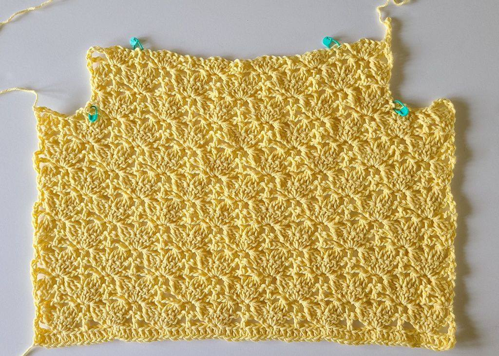 Yellow crochet crop top panel showing armhole shaping detail worked in textured stitch pattern.