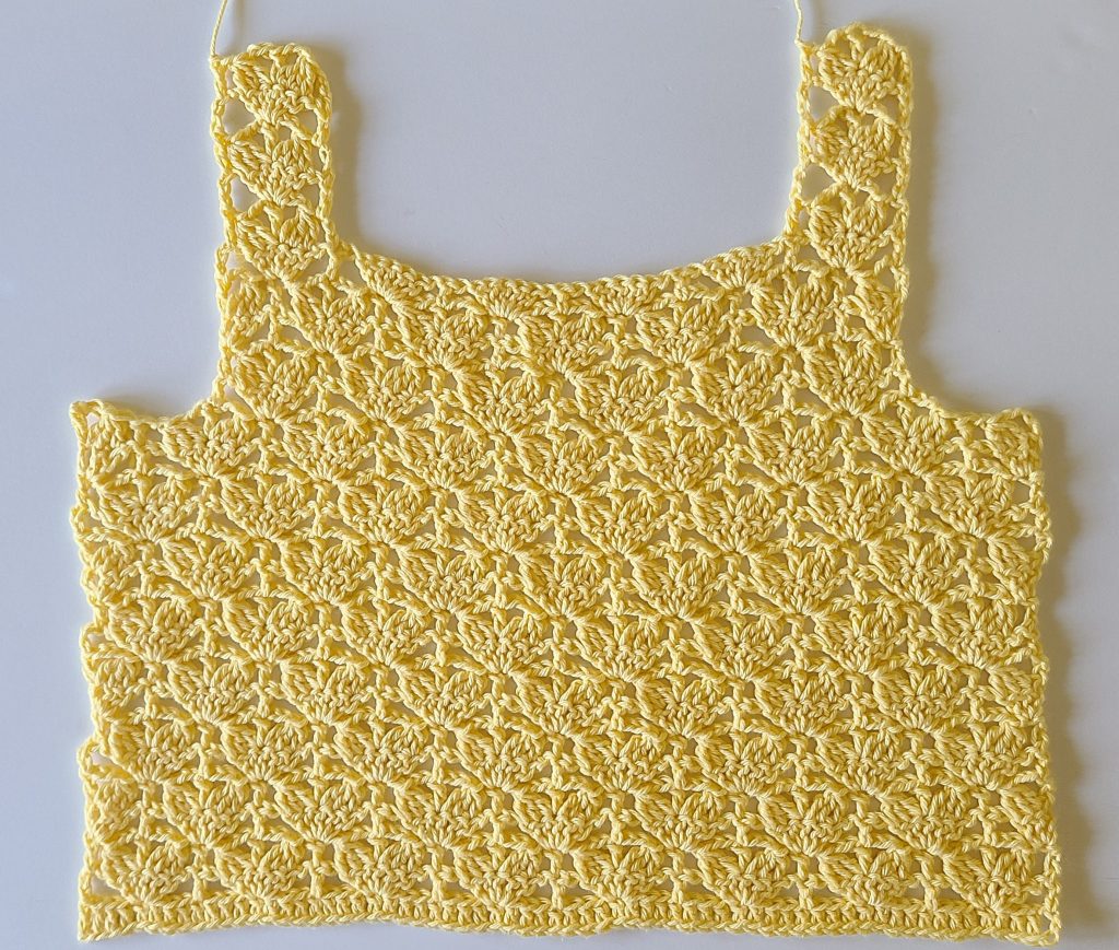 Yellow crochet crop top panel with shoulder straps attached, laid flat on a white surface.