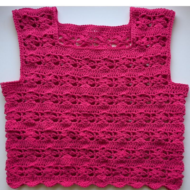 Finished Zana crochet top hanging on a wooden hanger, showcasing the floral stitch design and square neckline.