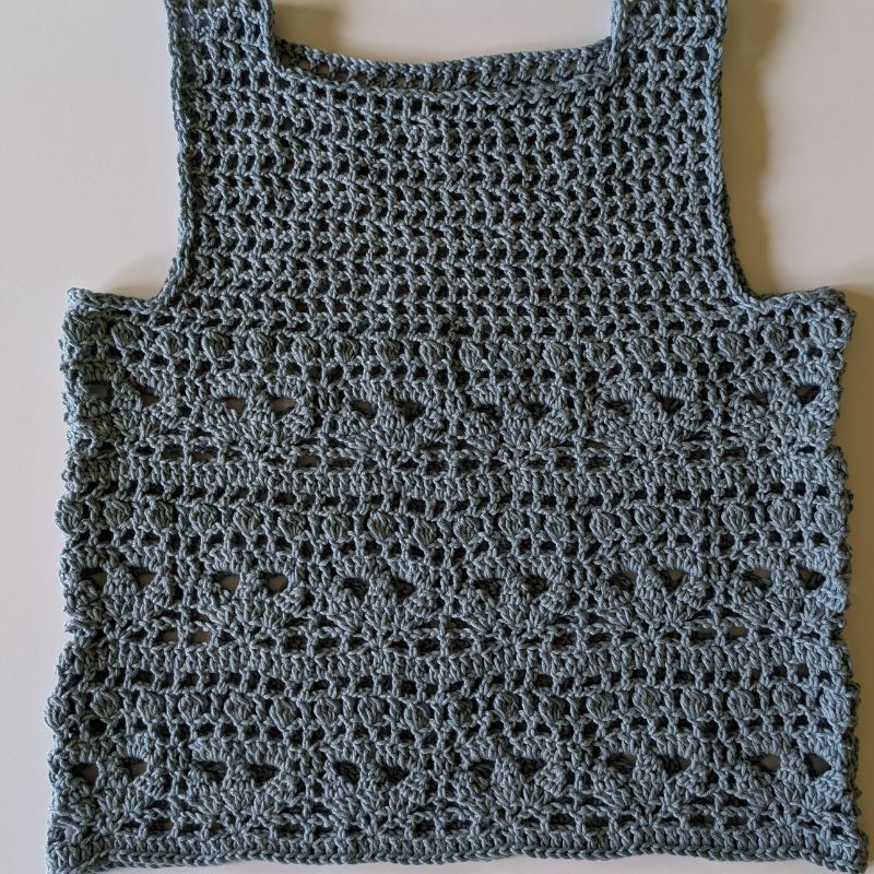 Finished Top made with an airy mesh yoke and floral lace stitch pattern, hanging on a wooden hanger.